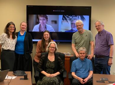 group photo: 7 white people in roomm and two on screen