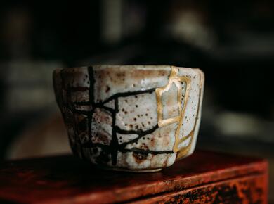 Kintsugi: a rough pottery cup with broken seams filled with gold