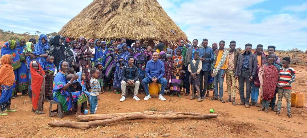 a group of people stand outside a hut with yellow water cans